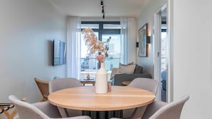 A modern dining area with a round table and six chairs, a vase with dried flowers, and a city view through large windows. - The Sage Aparthotel by Totalstay (CAPE TOWN)