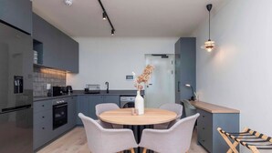 A modern kitchen with grey cabinets, a round wooden table, and grey chairs. - The Sage Aparthotel by Totalstay (CAPE TOWN)