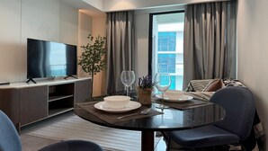Et moderne hotelværelse med et fladskærms-tv, et spisebord dækket med tallerkener og glas, en sofa og et stort vindue med gardiner.