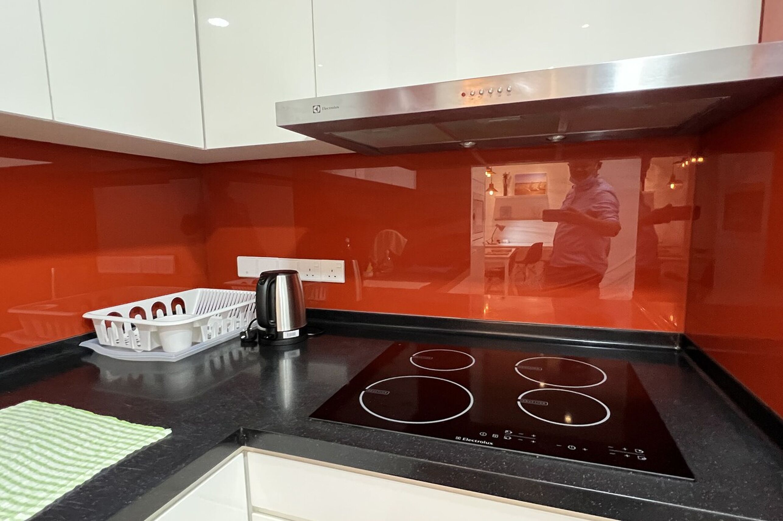 A modern kitchen with a black induction cooktop, a stainless steel range hood, and a white dish rack.