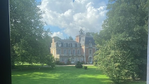 Un grand bâtiment historique à la façade symétrique, entouré de pelouses bien entretenues et d’arbres majestueux.