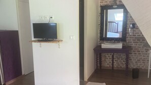 Une pièce avec un plancher en bois, un téléviseur posé sur un meuble en bois, un miroir au-dessus d’un lavabo et un escalier menant à l’étage supérieur.