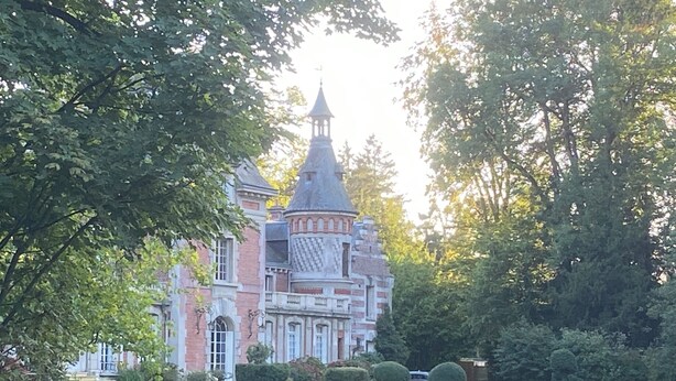 Un grand bâtiment historique, doté d’une tour imposante et d’un jardin bien entretenu, avec des haies taillées.