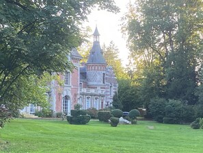 Un edificio grande e histórico con una torre destacada y un jardín bien cuidado con setos podados.