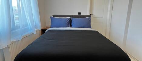 Un dormitorio moderno con una cama, un reposapiés gris e iluminación empotrada en el techo.