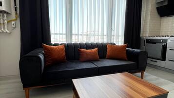 A modern living room with a black sofa, orange cushions, and a wooden coffee table.