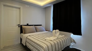 A modern bedroom with a bed, a black ottoman, and a window with black curtains. - LİGHTHOUSE SUİTE (Atakum)