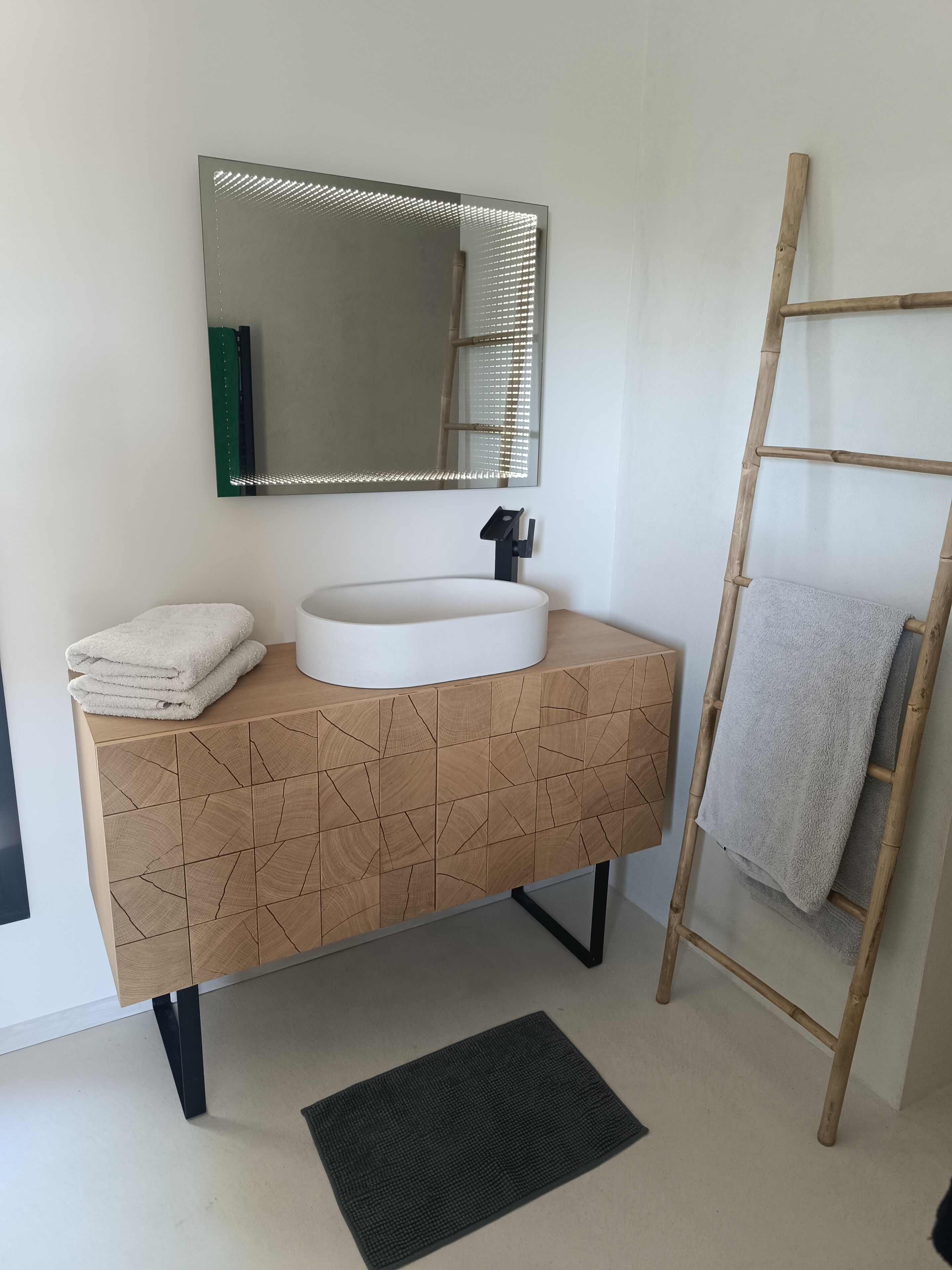 A bathroom with a white sink, a mirror, a towel rack, and a wooden ladder.
