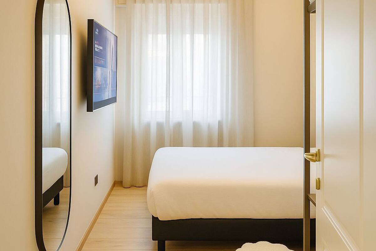 A bedroom with a bed, a mirror, a television, and a window with curtains.