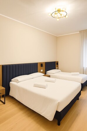Ein Hotelzimmer mit zwei Betten, einem Nachttisch aus Holz, einer modernen Chandelierleuchte und einem Fenster mit Vorhängen.