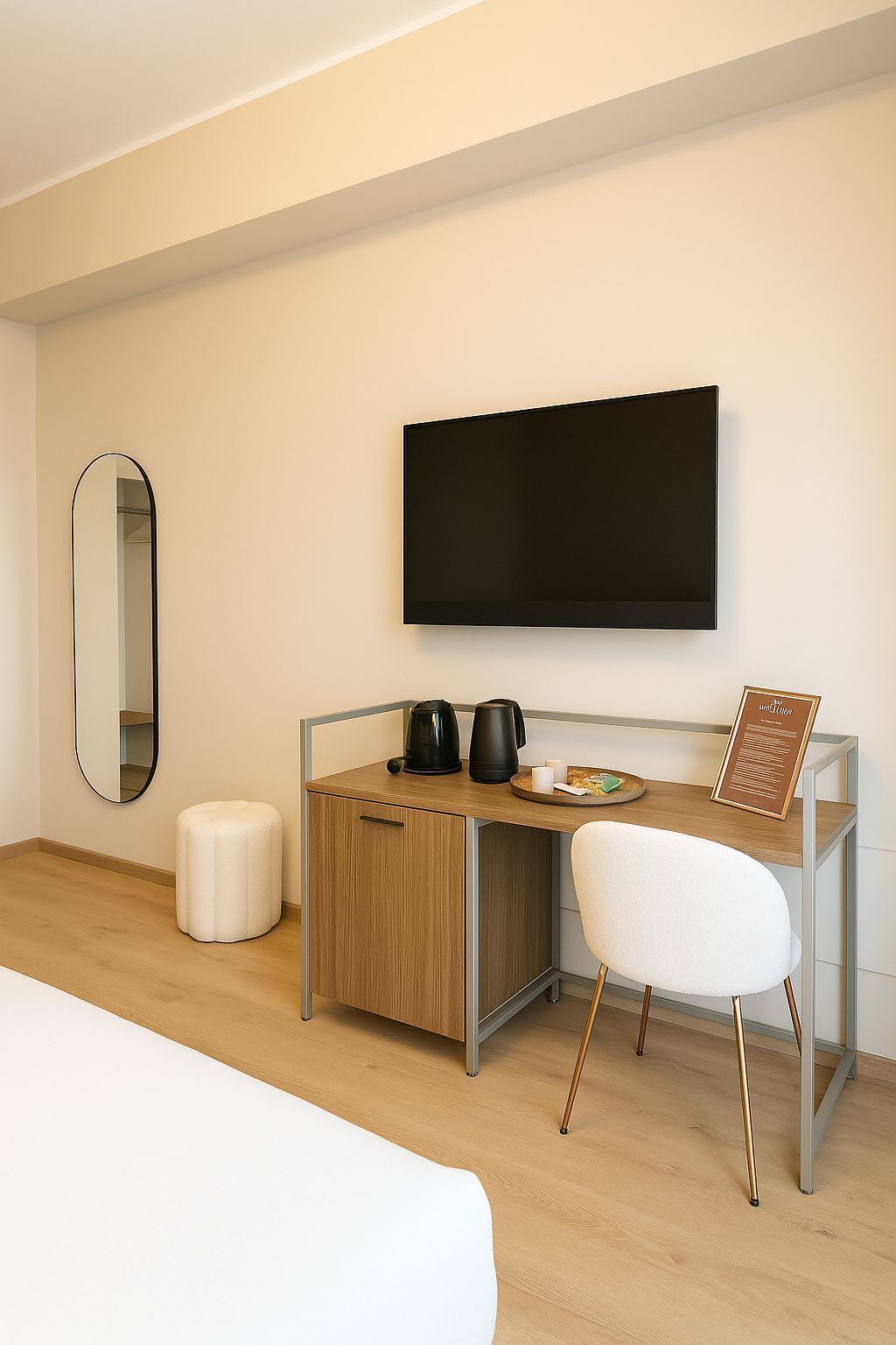 A modern hotel room with a wooden desk, a white chair, a flat-screen TV, a round table with a coffee maker, a kettle, and a breakfast plate.