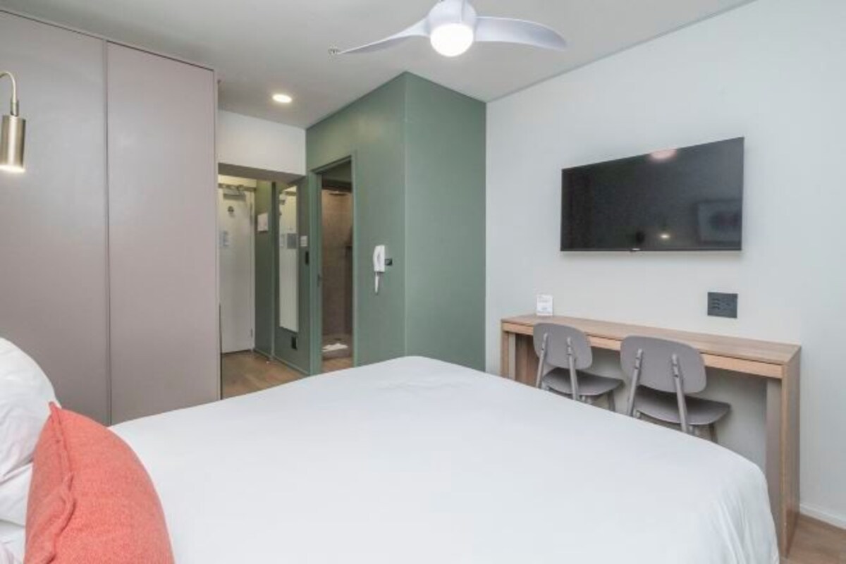 Een slaapkamer met een bed, een bureau met stoelen, een televisie en een kledingkast.