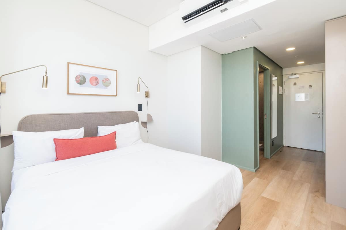 Quarto de hotel moderno com uma cama grande, uma obra de arte emoldurada acima da cama e uma porta que dá para o banheiro.