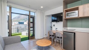 A modern apartment with a dining area, kitchenette, and a large sliding glass door leading to a balcony with a mountain view. - Habitat Aparthotel by Totalstay (Cape Town)