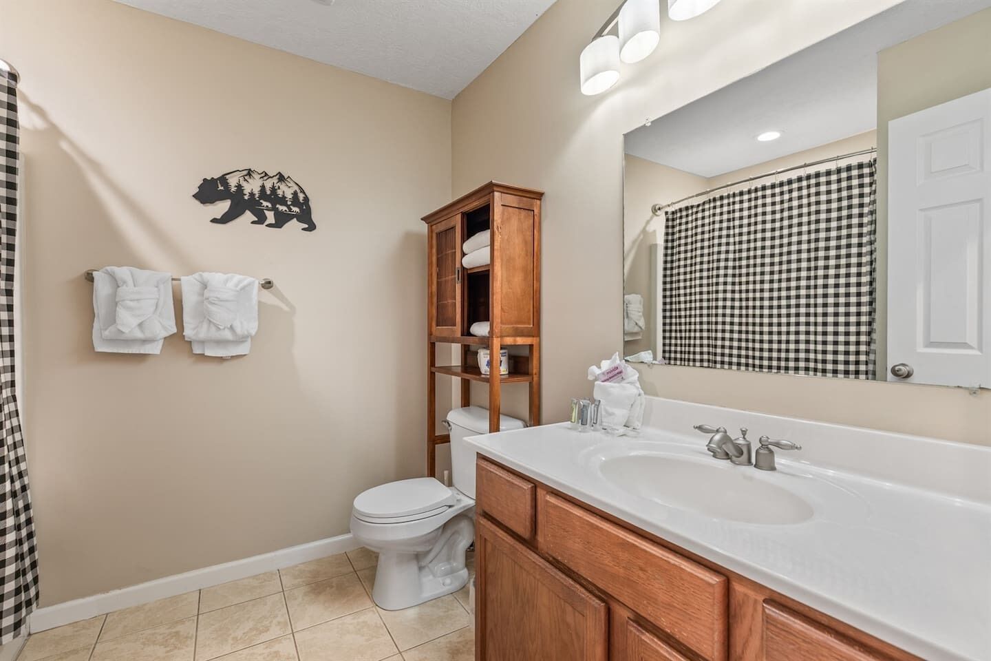A bathroom with a toilet, a wooden cabinet, a sink, and a mirror.