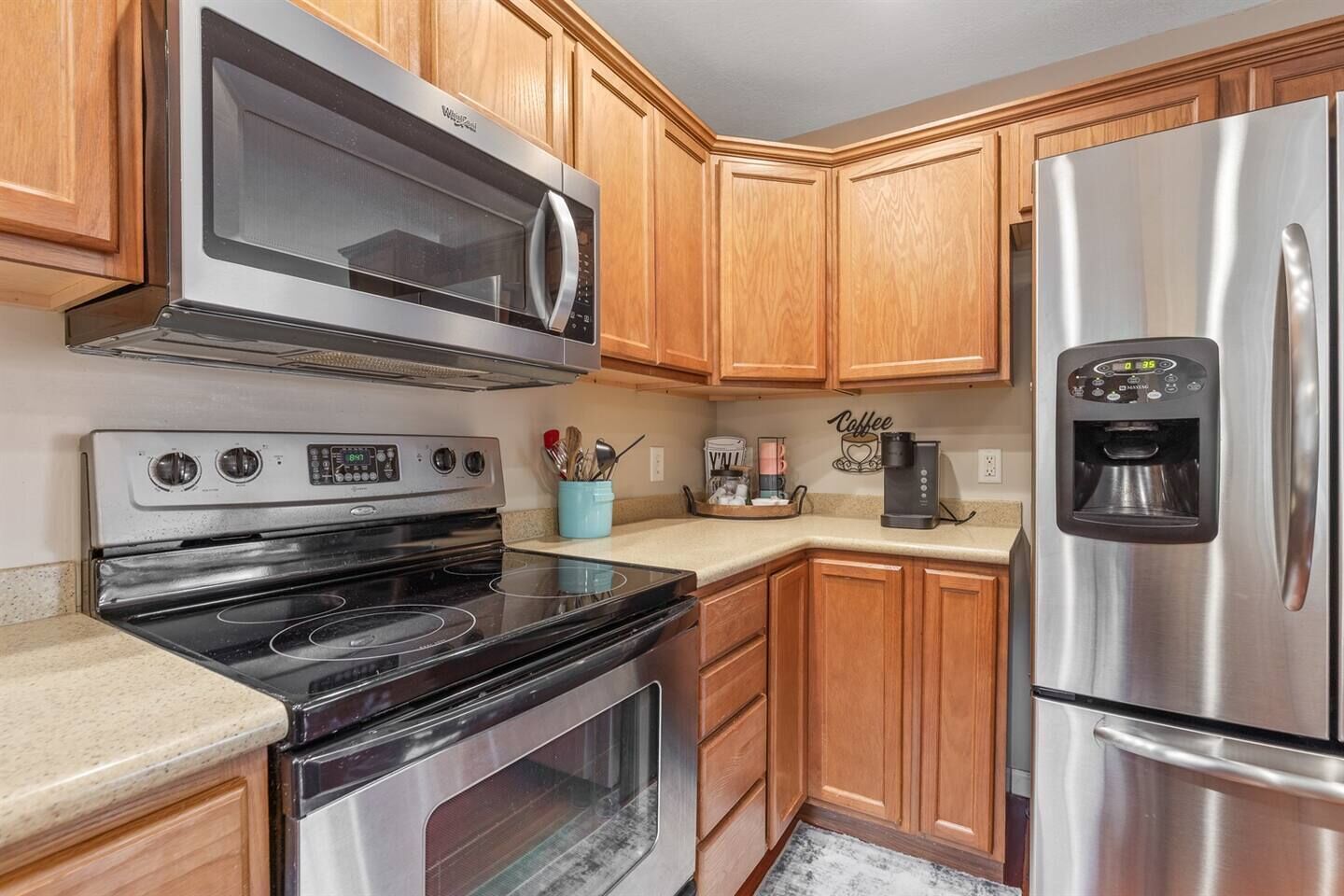 A kitchen with wooden cabinets, a stainless steel microwave, a stove, and a refrigerator.