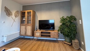 Un salon avec un meuble en bois, un téléviseur et une grande plante.