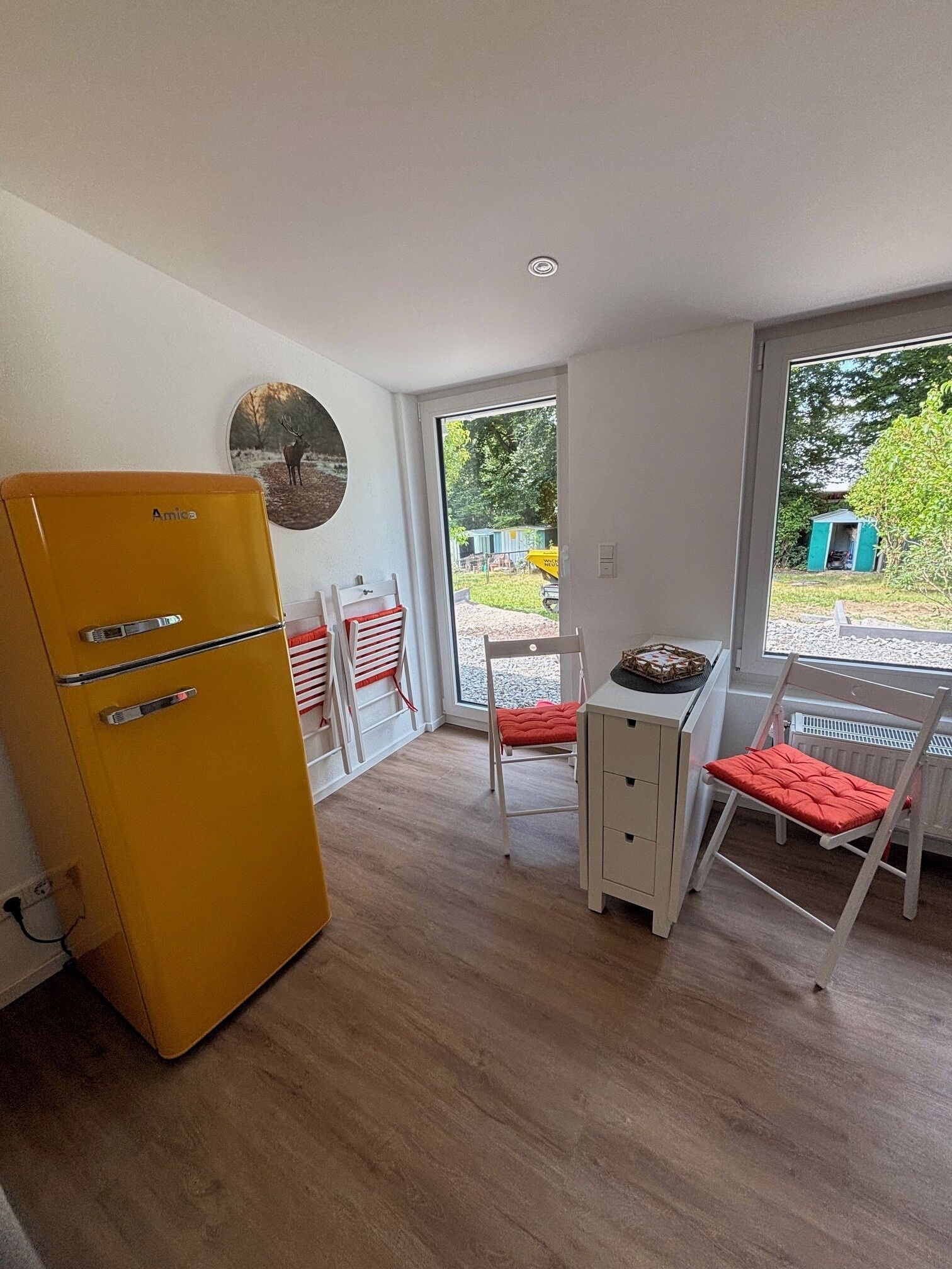 Habitación pequeña con un refrigerador amarillo, una mesita con una silla y una ventana que ofrece vistas al exterior.