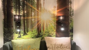 Une pièce dont un mur est décoré d’une fresque sur le thème de la forêt, avec deux lampes fixées au mur et deux coussins sur lesquels est inscrit le mot « Nature ».