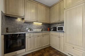 Een keuken met lichte houten kastjes, een granieten aanrechtblad, een inbouwoven en een magnetron.