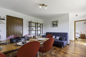 A dining area with a wooden table, red chairs, and a blue sofa. There are shelves with decorative items and a painting on the wall.