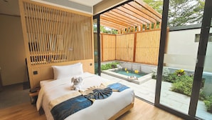 A modern bedroom with a large bed, a small bedside table, a wooden headboard, and a view of a garden and outdoor area.