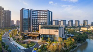 A modern hotel with a glass facade, surrounded by greenery and a river.