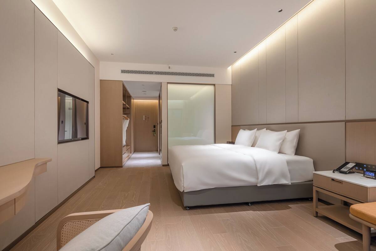 A modern hotel room with a bed, bedside table, and a mirror.