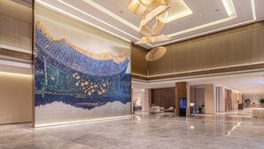 A spacious lobby with a large decorative wall, modern lighting fixtures, and a polished marble floor.
