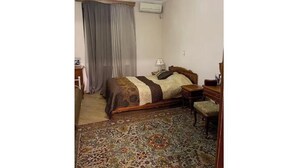 A bedroom with a bed, a nightstand, a chair, a desk, and a patterned rug. - Your apartment next to Yerevan State University (Martuni)