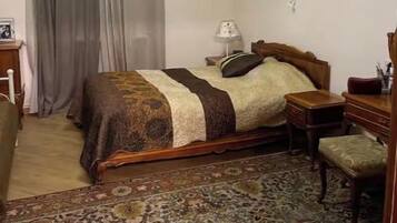 Un dormitorio con cama, mesita de noche, silla, escritorio y una alfombra estampada.