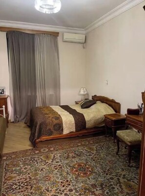 A bedroom with a bed, a nightstand, a chair, a desk, and a patterned rug. - Your apartment next to Yerevan State University (Martuni)