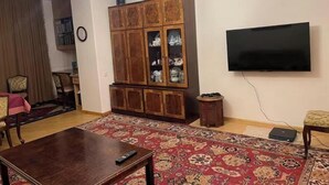 A living room with a wooden cabinet, a flat-screen TV, a chandelier, and a patterned carpet. - Your apartment next to Yerevan State University (Martuni)