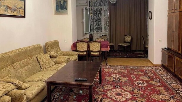 A living room with a sofa, a coffee table, a chandelier, a dining area with chairs, and a patterned rug. - Your apartment next to Yerevan State University (Martuni)