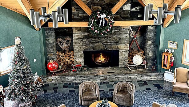 A cozy interior with a stone fireplace, wooden beams, and a Christmas tree. - 1BR | Balcony over the Pemi River | Loon Views | Indoor Pool & Hot Tub (Lincoln)