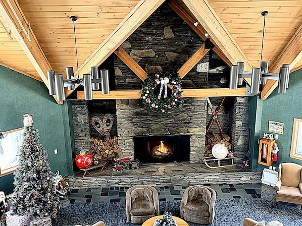 A cozy interior with a stone fireplace, wooden beams, and a Christmas tree.