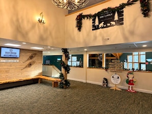 A hotel lobby with a wooden bench, Christmas decorations, a sign for 'Solid Ground Construction', and directional signs for various hotel areas.