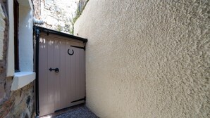 A narrow alleyway with a beige door, a stone wall, and a gravel path.