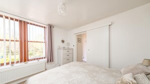 A bedroom with a large bed, a dresser, a radiator, and a window with curtains.