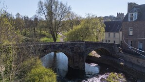 A stone bridge over a river with a path leading to a building with a tower.