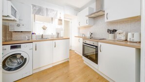 A modern kitchen with white cabinetry, a built-in oven, a microwave, and a washing machine.