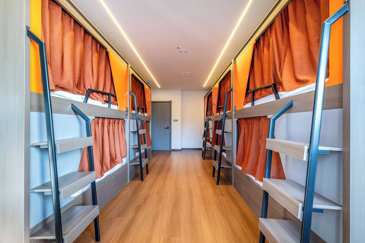 Un couloir avec des lits superposés et des rideaux orange.