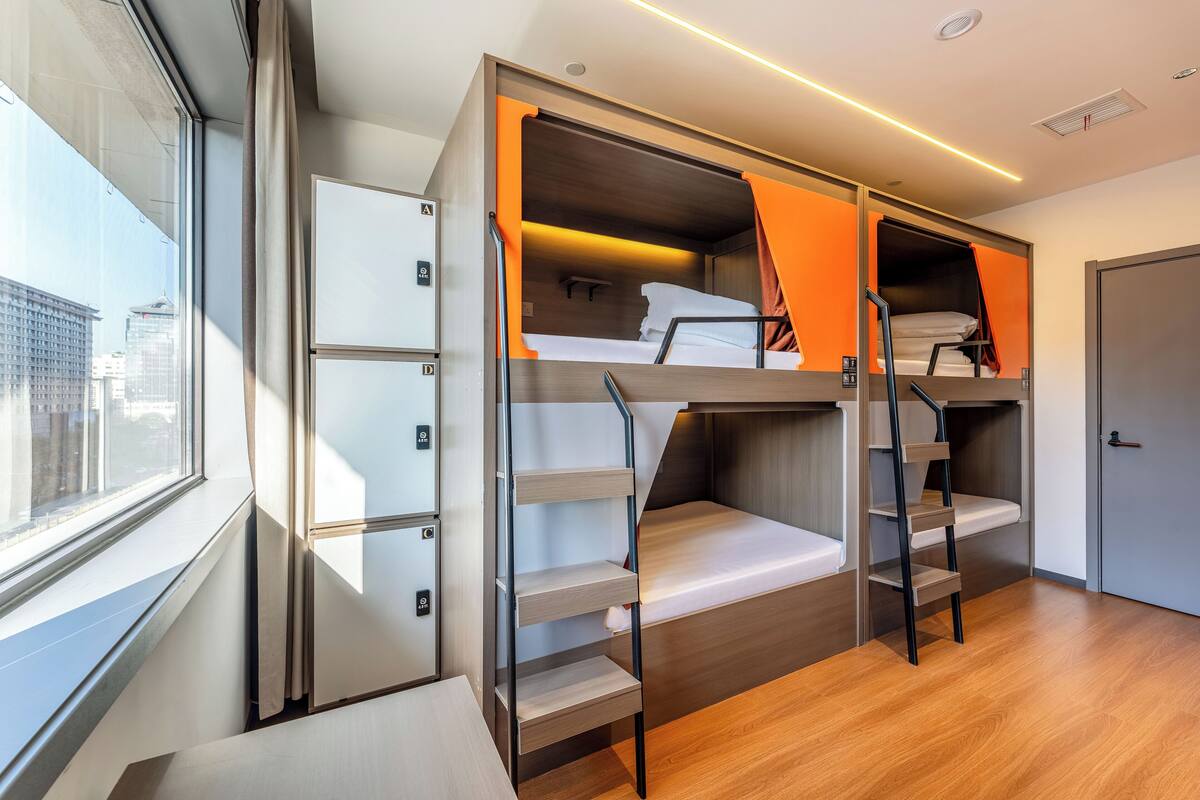 Une chambre d’hôtel moderne équipée d’un lit superposé, d’un bureau et d’une fenêtre donnant sur la ville.