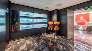 Un moderno vestíbulo de hotel con piso de mármol, pantallas digitales en la pared mostrando información y un mostrador de recepción con un detalle en pared rojo.