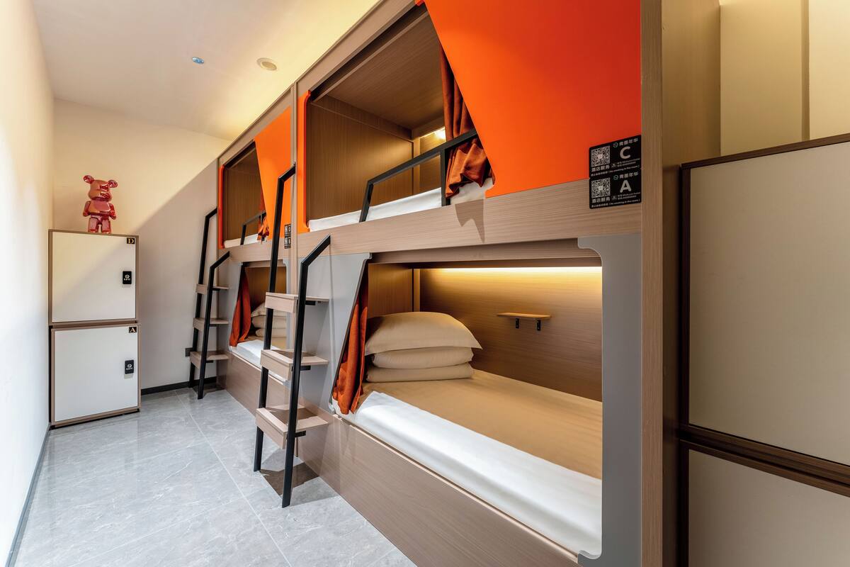 Une chambre avec des lits superposés, un petit réfrigérateur, une armoire en bois et une décoration représentant un ours sur le mur.