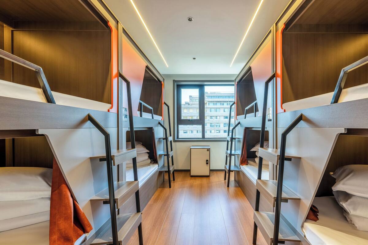 Une chambre avec des lits superposés, un plancher en bois, une petite fenêtre et un radiateur.