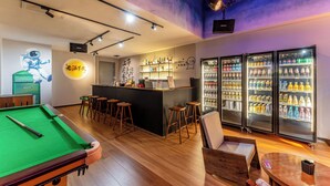 Mesa de billar, zona de bar, taburetes, asientos y refrigeradores llenos de bebidas.