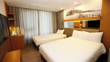 A hotel room with two beds, a desk, a TV, and a large window with curtains.