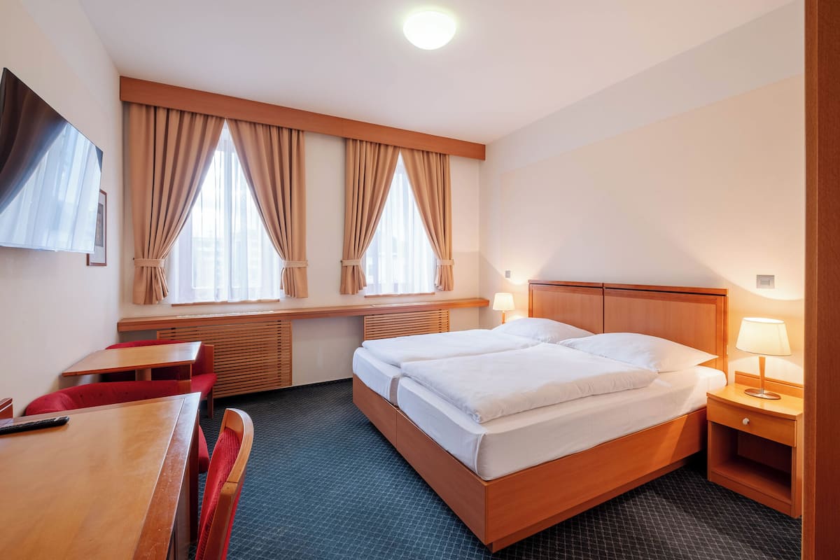 Habitación de hotel con cama doble, escritorio con silla, televisor y ventana con cortinas.