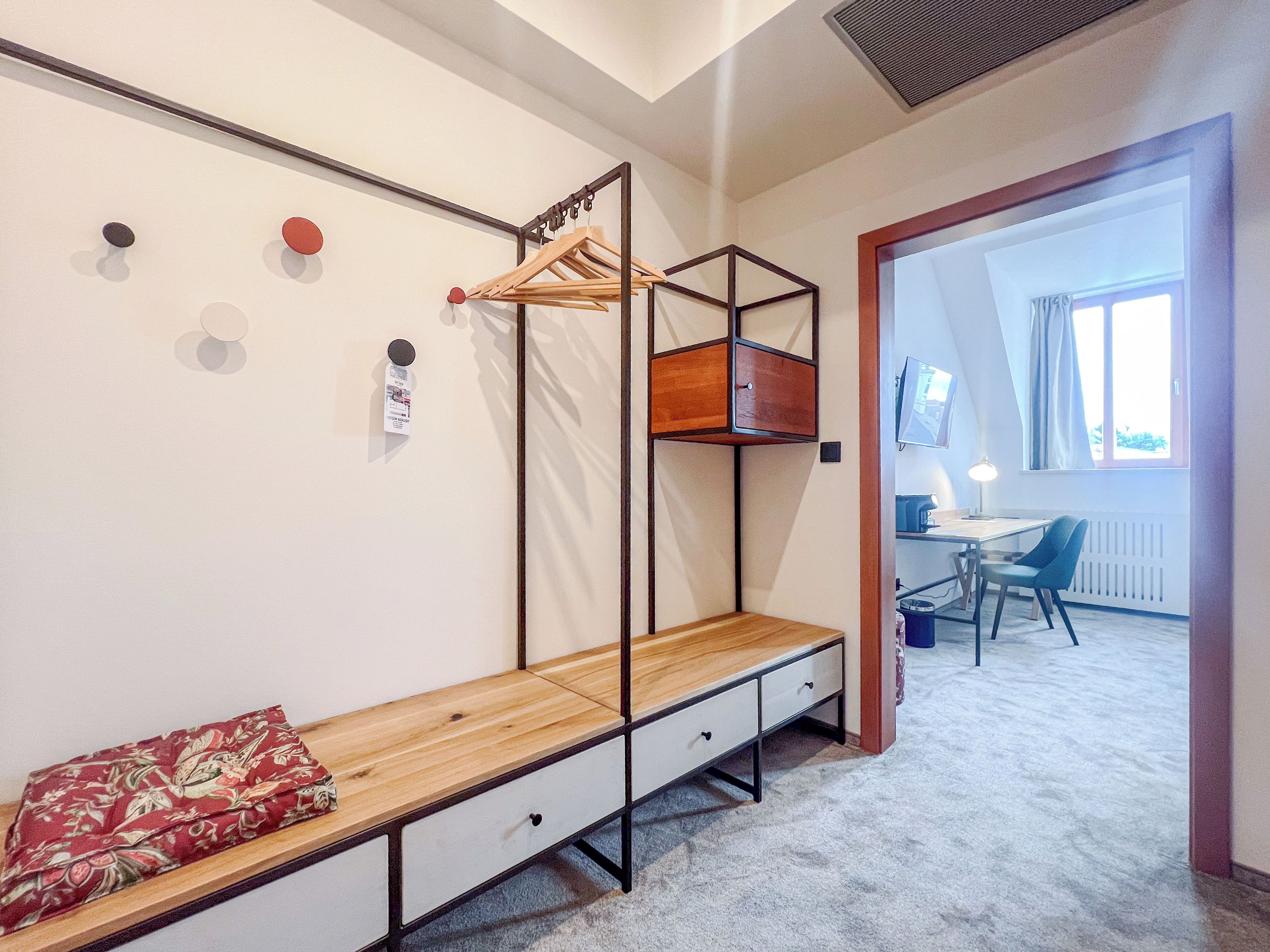 A bedroom with a wooden bed, a bench with drawers, a hanging clothes rack, and a desk with a chair.